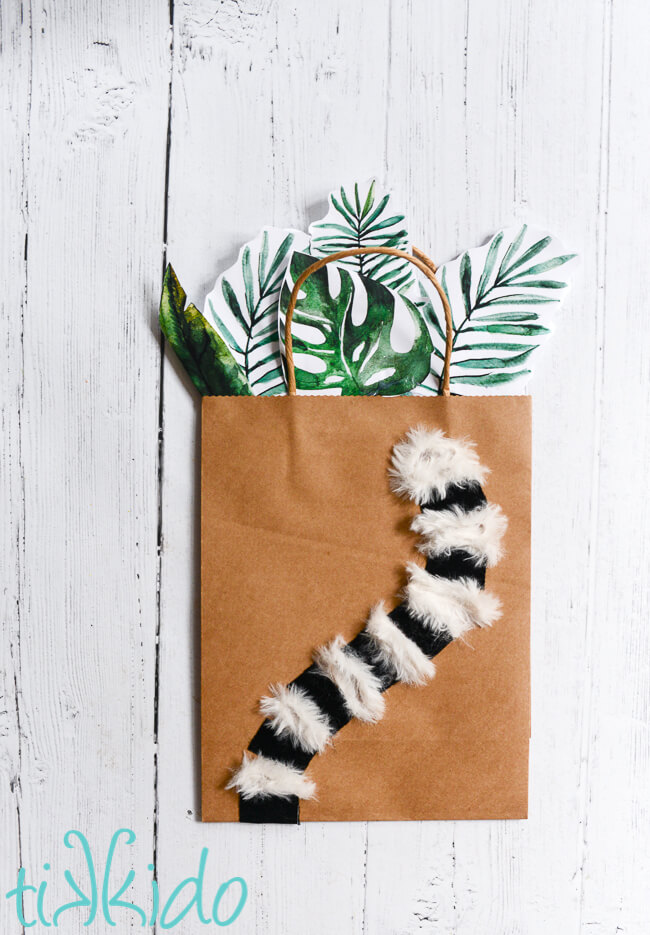 Lemur gift bag with a furry lemur tail decorating a plain brown kraft gift bag, and with paper tropical leaves sticking out of the top of the bag.