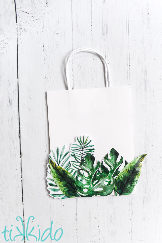 DIY Tropical Gift Bag made with free printable tropical leaves on a white wooden surface.