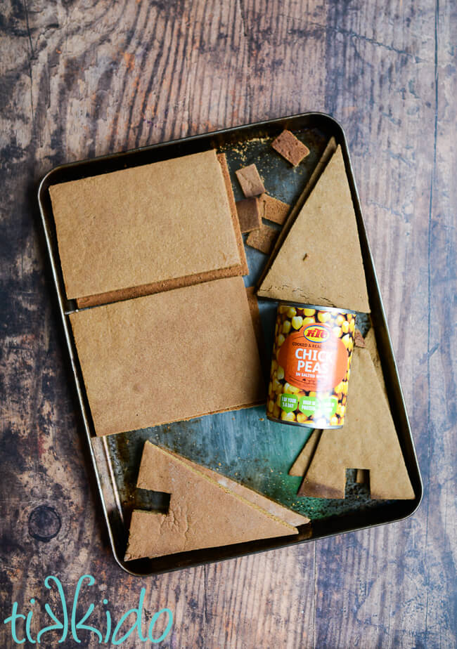 Pieces of a gingerbread house made with eggless, vegan gingerbread on a baking pan with a can of chickpeas.