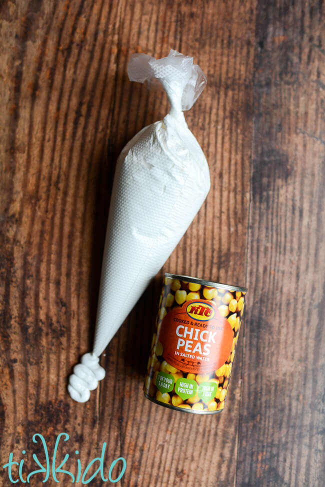 Eggless, vegan royal icing made with aquafaba in a piping bag next to a can of chick peas.
