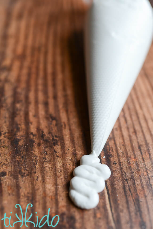 Eggless vegan royal icing being piped on a dark wooden surface.