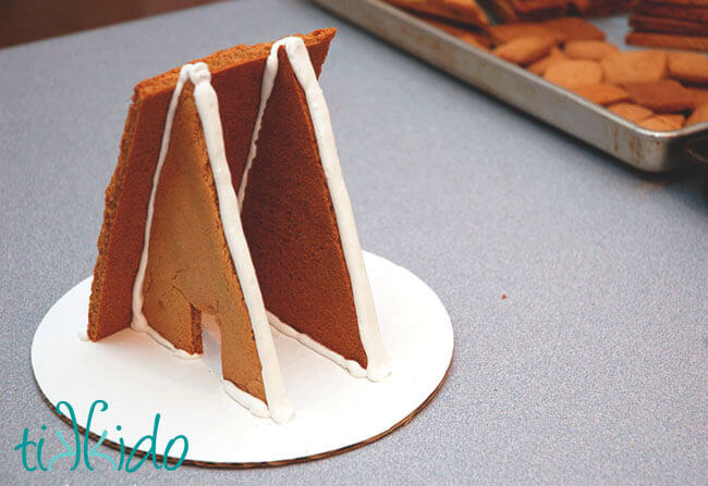 A frame gingerbread house being assembled with royal icing.