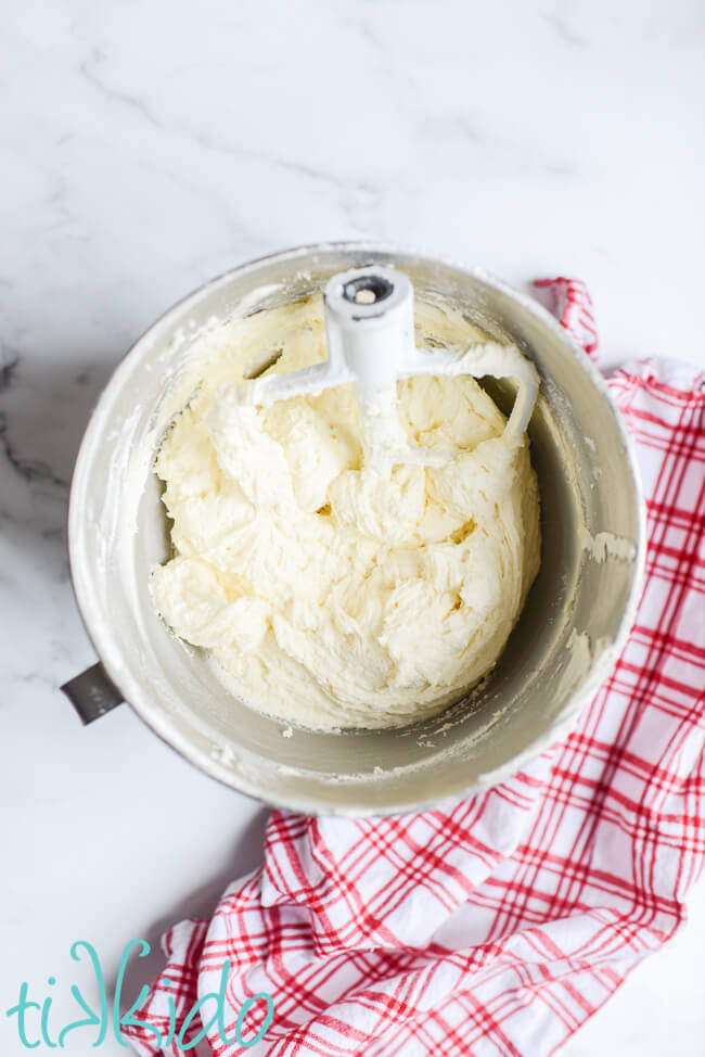 American Buttercream Frosting Recipe made in a Kitchenaid mixing bowl, next to a red and white checked kitchen towel.