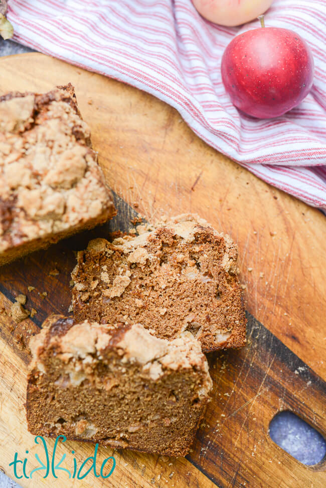 Closeup of two slices of crumb topped apple bread on a wooden cutting board.