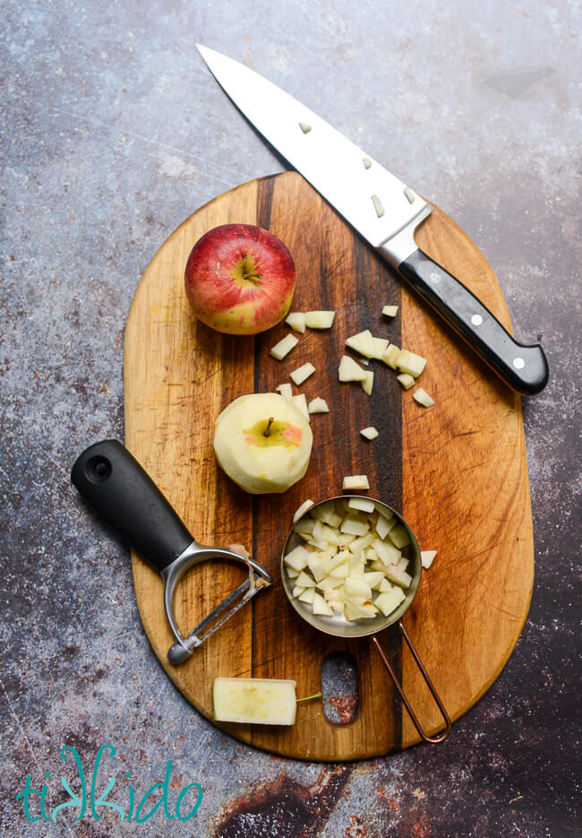 Apples being peeled and diced on a wooden cutting board.