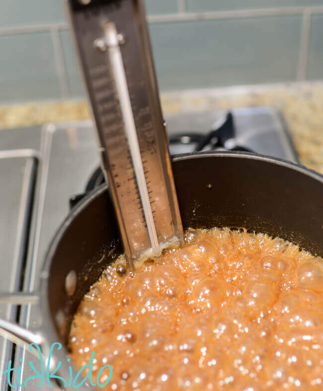 Apple Cider Caramels recipe ingredients cooking in a saucepan on the stove, with a candy thermometer.