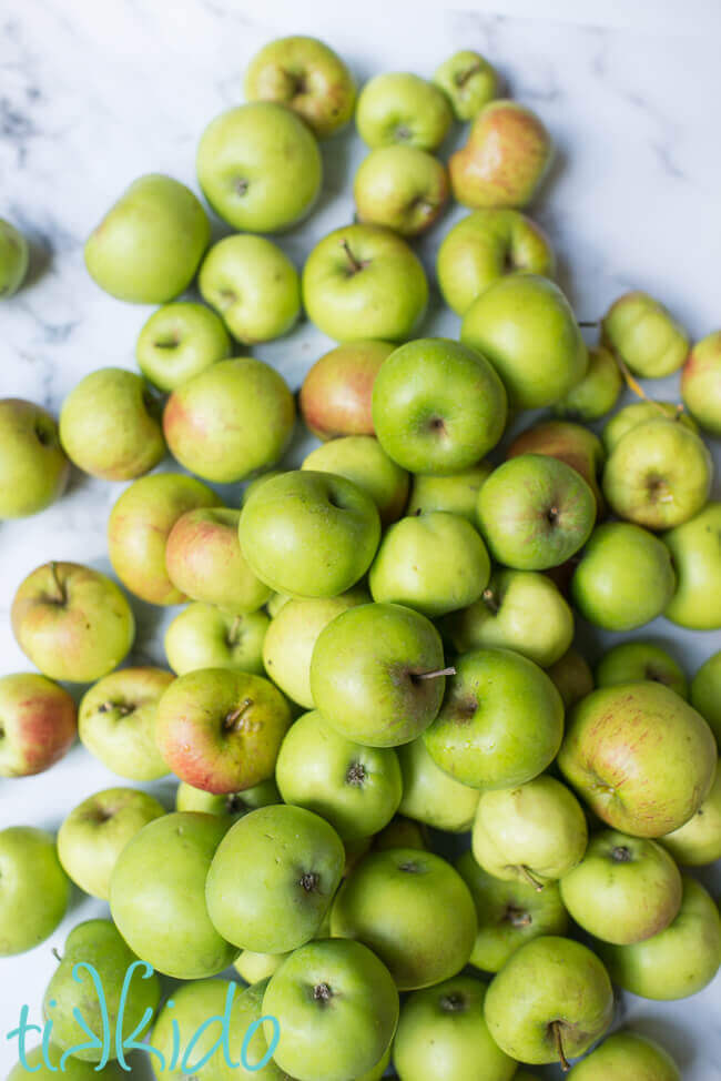 Pile of green apples on a white marble background.