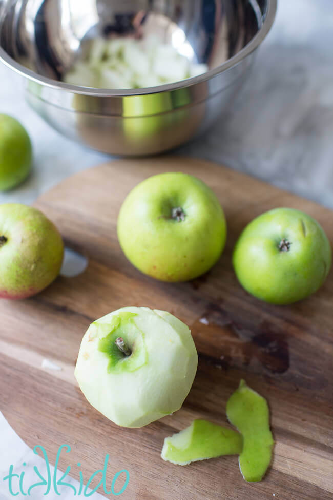 Green apples being peeled on a wooden cutting board.