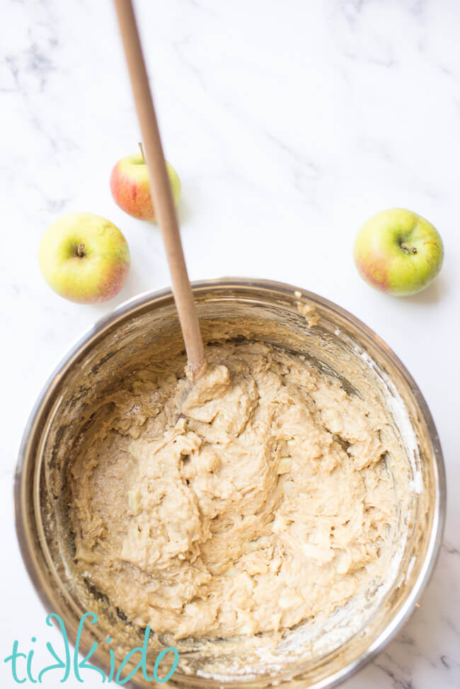 Apple muffin batter for making apple muffin recipe in a silver bowl with a wooden spoon.