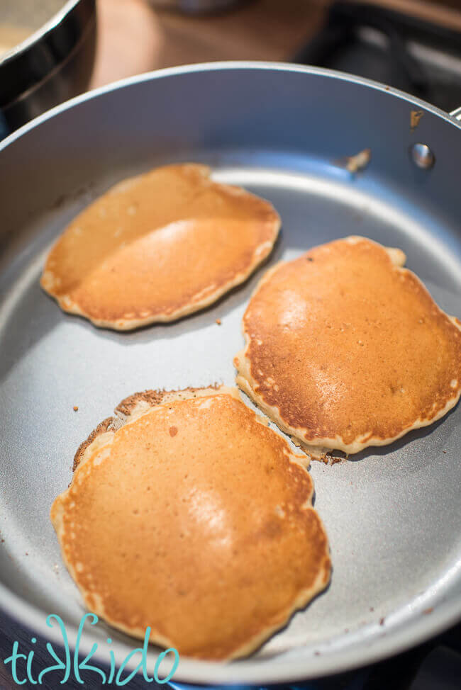 Three apple pancakes being cooked in a frying pan.