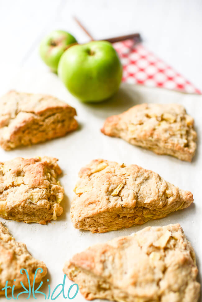 Freshly baked apple scones on a baking sheet lined with parchment paper, with fresh apples in the background.