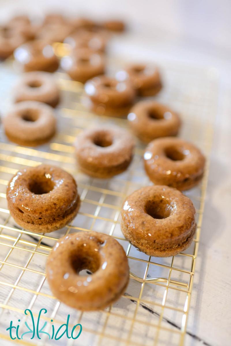 Freshly baked apple cider donuts dipped in apple cider glaze, and drying on a golden cooling rack.