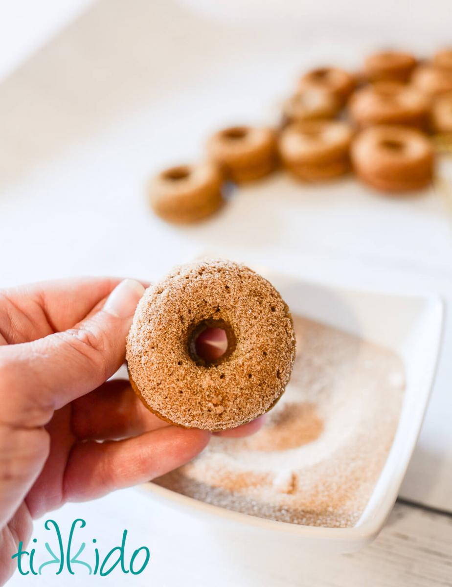 Baked apple cider donut being dipped in cinnamon sugar.