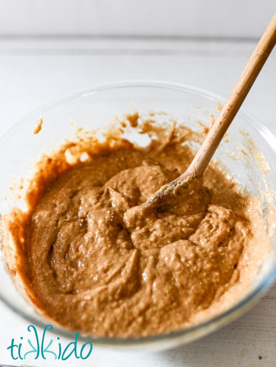 Batter for apple cider donuts mixed with a wooden spoon in a glass mixing bowl.