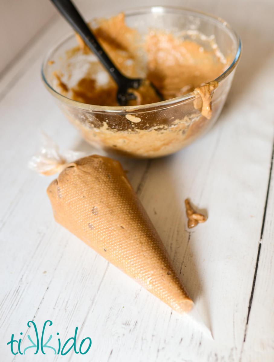 Apple cider doughnut batter in a glass mixing bowl and in a disposable piping bag on a white wooden surface.