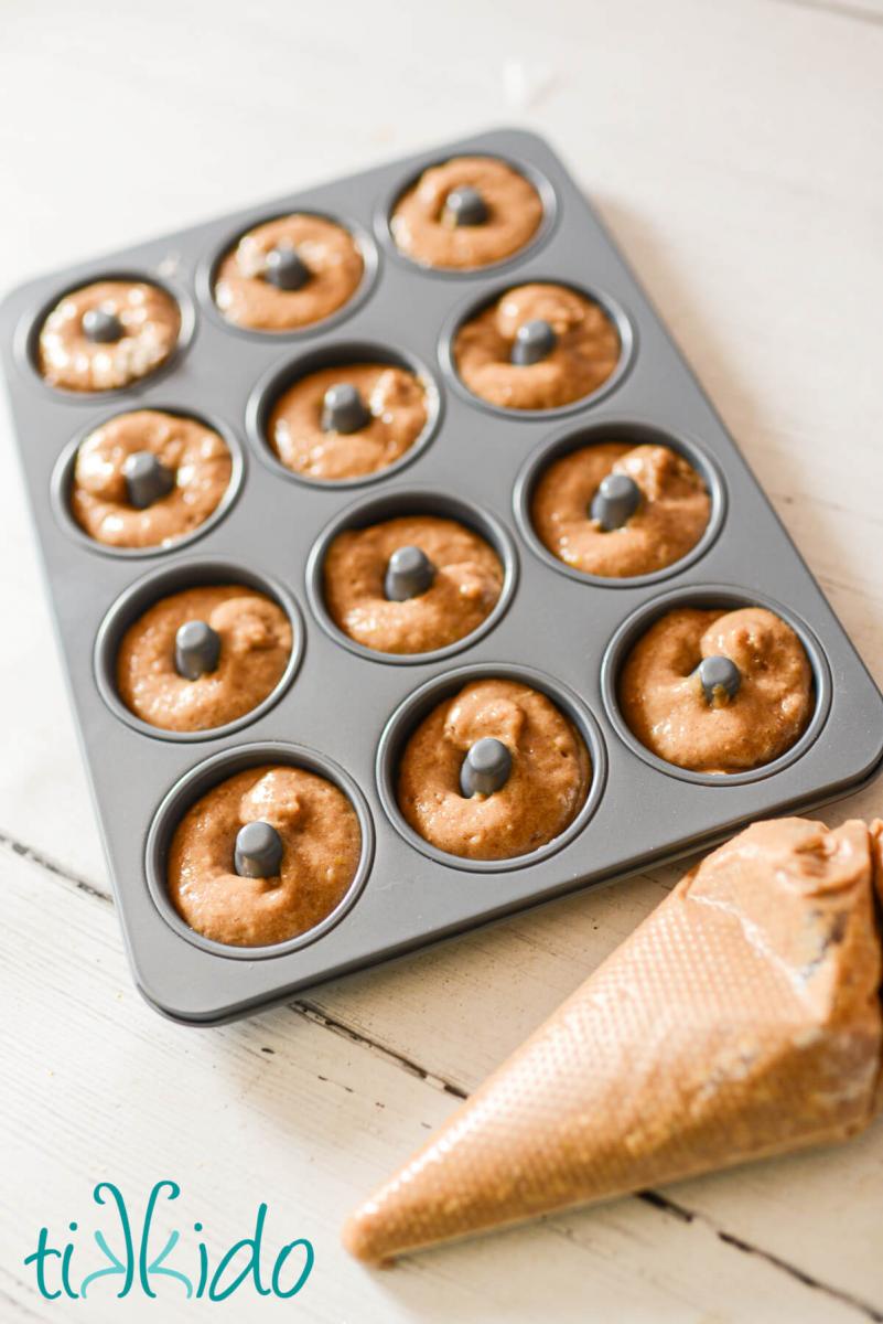 Batter for apple cider donuts being piped from a disposable piping bag into a doughnut baking tray.
