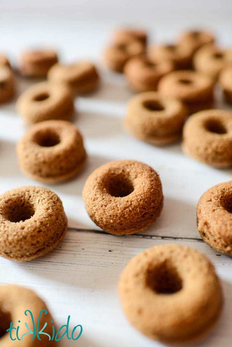 Freshly baked apple cider doughnuts cooling on a white wooden surface.