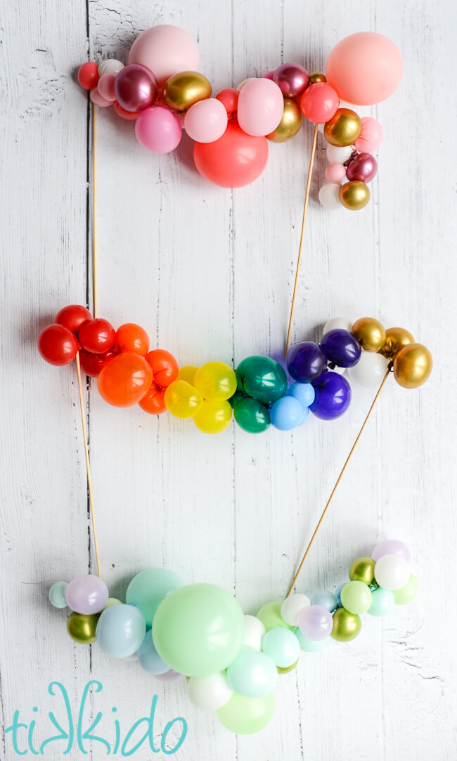 Three miniature balloon garland cake toppers on a white wooden background.
