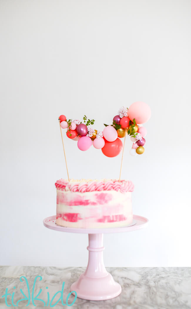 Balloon Garland Cake Topper made with pink and gold miniature balloons, on top of a pink cake on a pink cake stand.