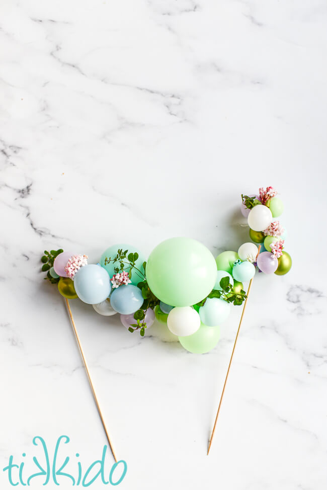 Mini Balloon Garland Cake Topper with fresh flowers on a white marble surface.