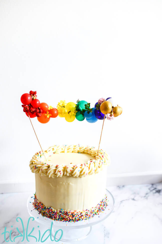 Mini balloon garland cake topper in rainbow colors on a cake decorated with rainbow sprinkles.