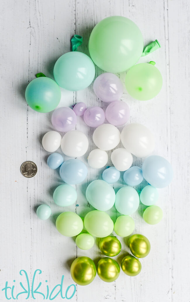 Miniature balloons in green, blue, and white tones, next to a quarter for scale.