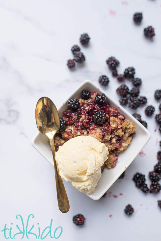 blackberry crisp with a scoop of vanilla ice cream in a white bowl.