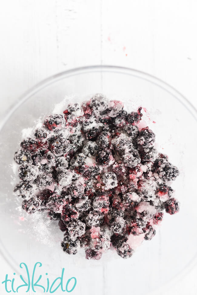 Blackberries and sugar in a clear bowl on a white wooden surface, for making Blackberry Gin Recipe.