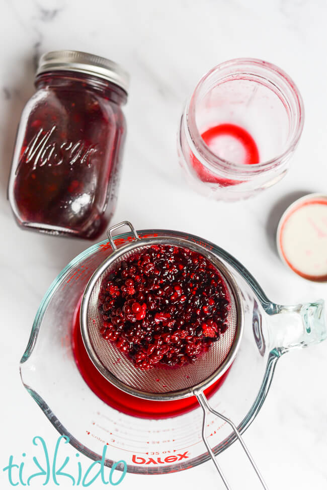 Blackberries being strained from the homemade blackberry gin into a large pyrex measuring cup.