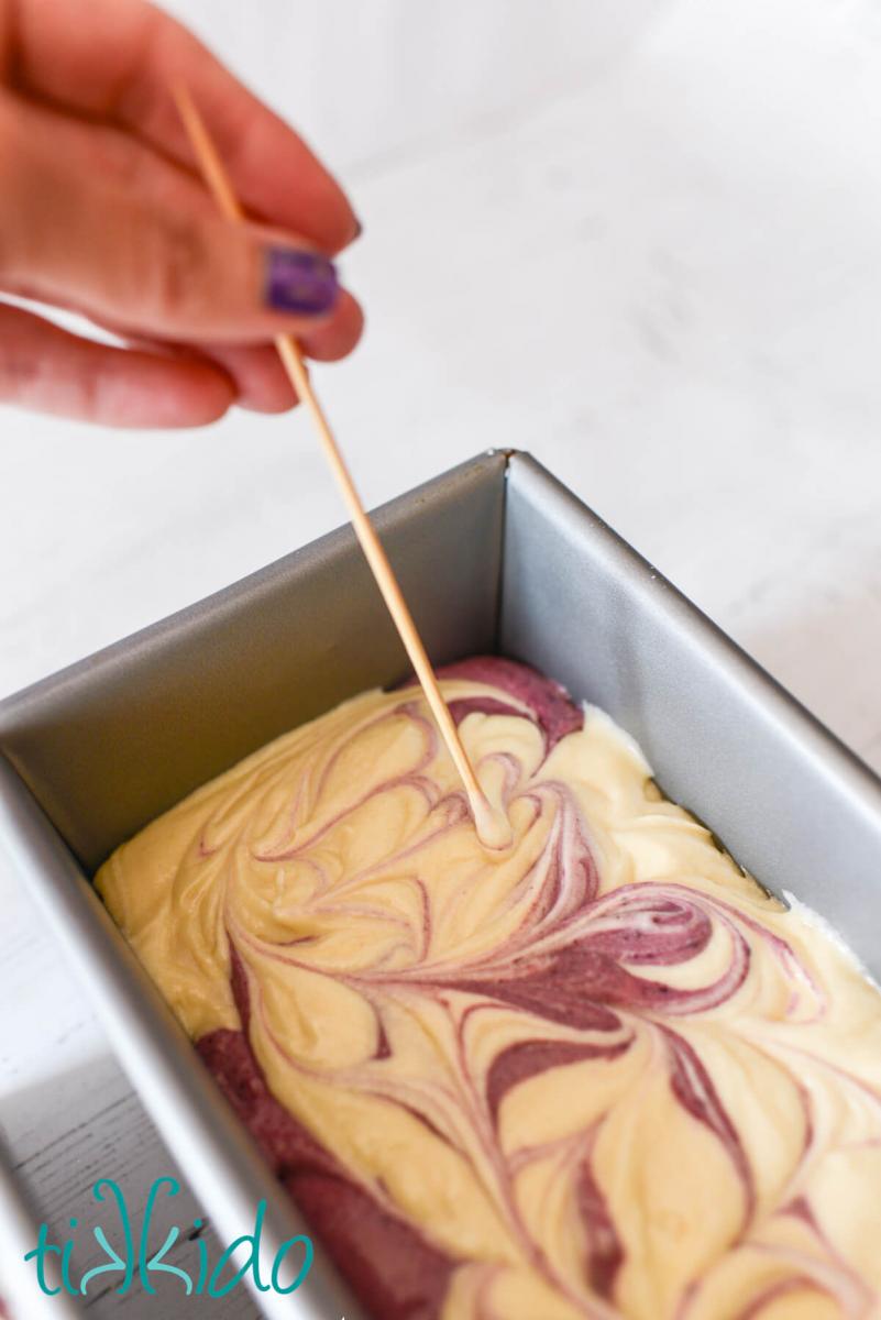 Blackberry Pound Cake Recipe Blackberry and vanilla pound cake batter being swirled together in a bread loaf pan with a bamboo skewer.