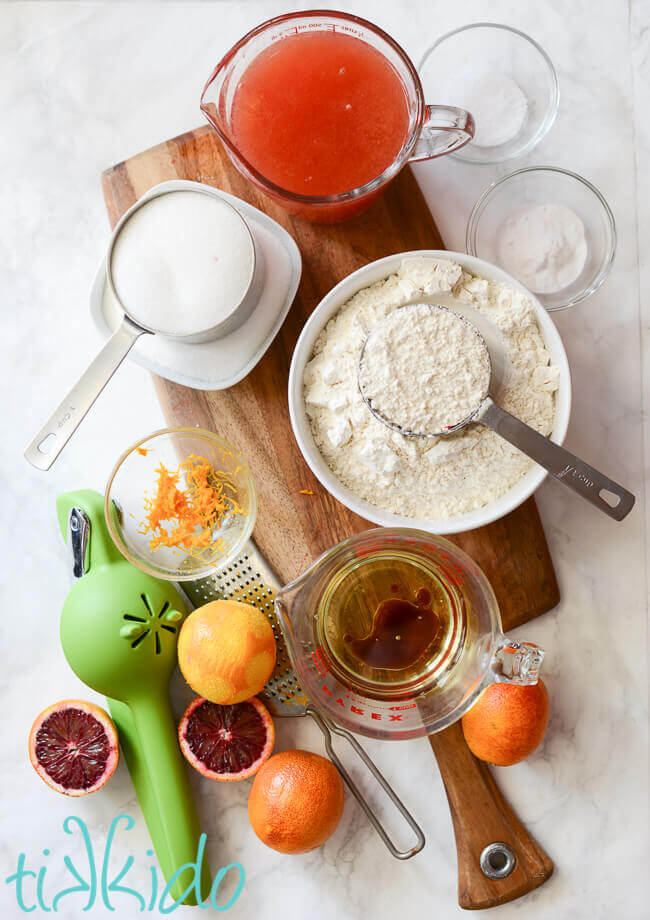 Ingredients for blood orange cupcakes on a wooden cutting board on a white marble surface.