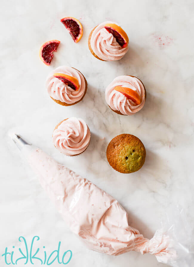 Light pink Blood orange frosting being piped on blood orange cupcakes.