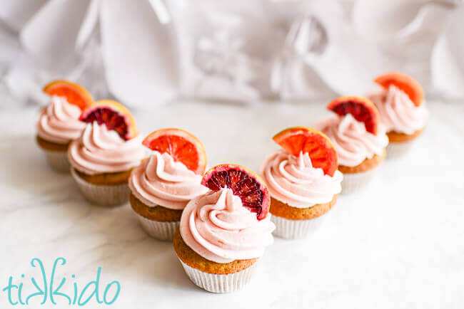 Blood orange cupcakes topped with blood orange frosting and slices of blood orange in a V formation