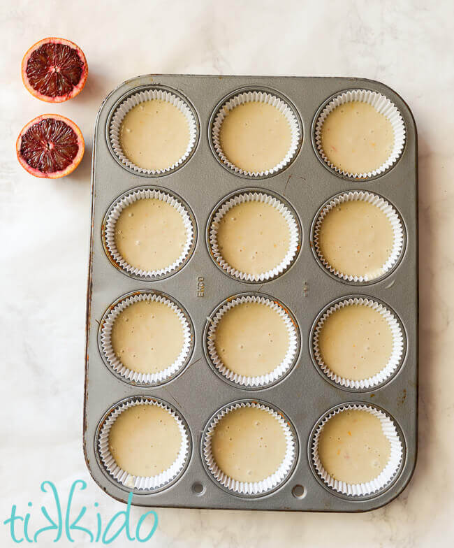 Blood orange cupcake batter in lined cupcake tins, next to a blood orange sliced in half.