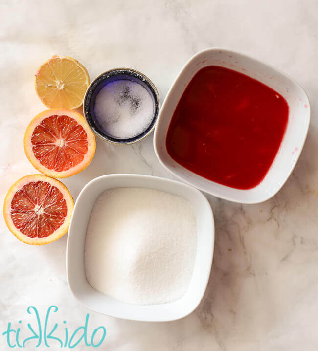 Blood orange simple syrup ingredients on a white marble background.