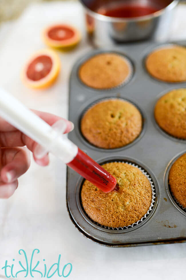 Blood orange simple syrup being injected into blood orange cupcakes.