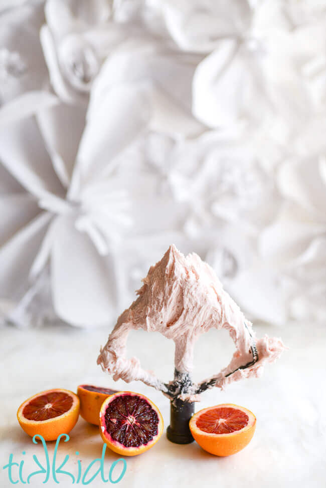 Light pink blood orange icing on a metal beater, surrounded by cut blood oranges.