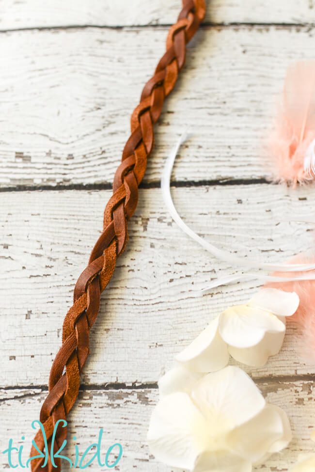 Leather lacing braided for boho gift wrapping, next to silk flowers and feathers on a white wooden surface.