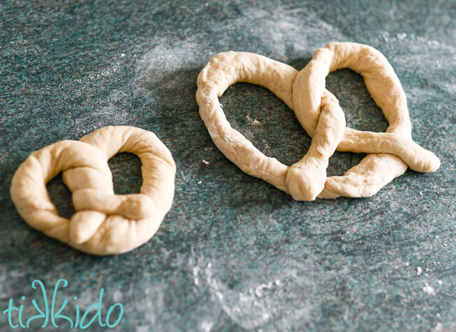 One small and one large unbaked pretzel on a lightly floured work surface.