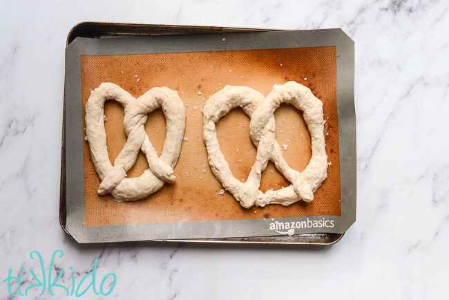 Unbaked Auntie Anne's copycat pretzels on a lined baking sheet, sprinkled with sea salt.