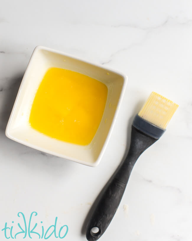 Small white bowl of melted butter next to a silicone basting brush.