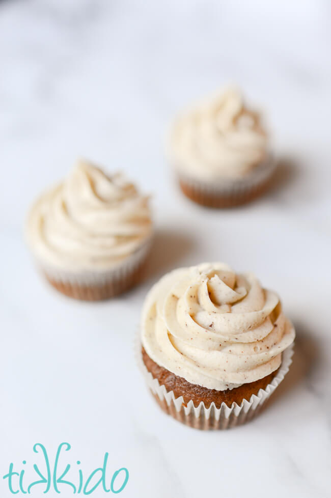 Browned Butter Frosting swirled on three banana cupcakes on a white marble surface.