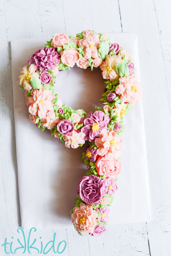 Cupcake cake in the shape of a number 9, decorated with American buttercream icing flowers in various shades of pink and purple.