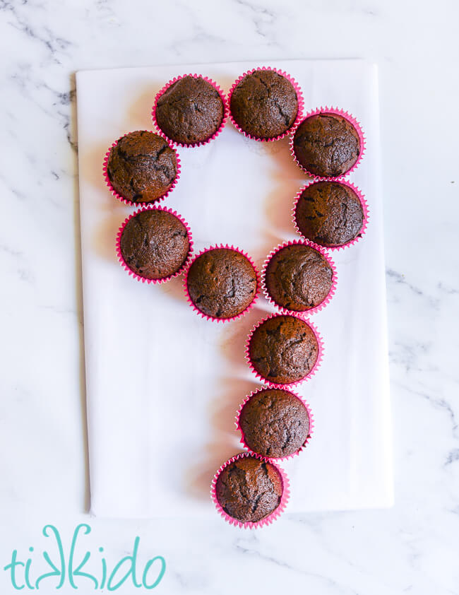 Chocolate cupcakes arranged in the shape of a number 9 on a white cake board.