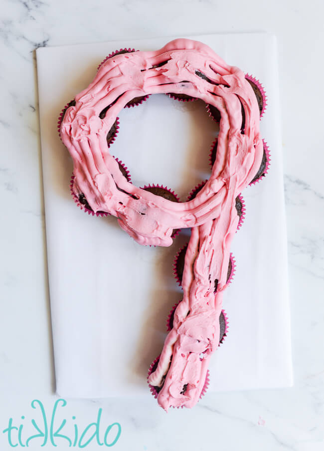 Pink icing covering the tops of chocolate cupcakes arranged in the shape of a number 9 to make a cupcake cake.