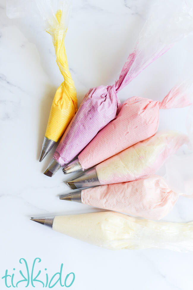 Six bags of buttercream icing in various shades of white, pink, purple, and yellow, for making buttercream icing flowers.