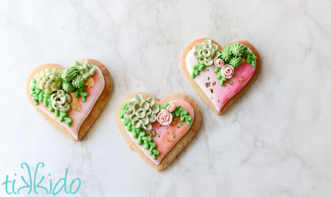 Heart shaped sugar cookies, covered in watercolor painted royal icing, with gold leaf and piped succulents.