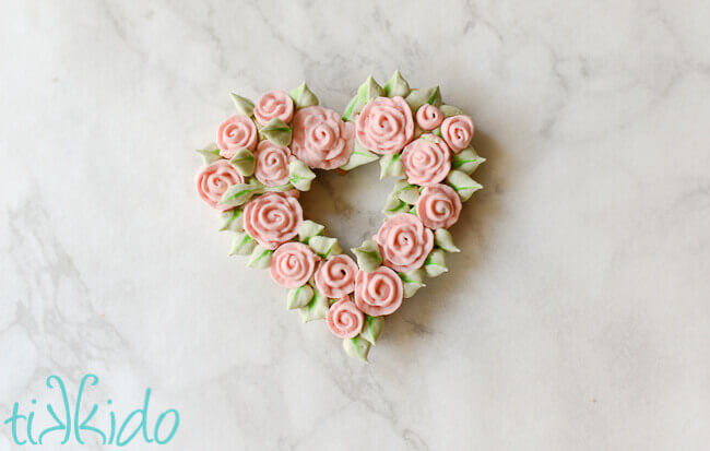 Heart shaped sugar cookie covered in piped royal icing roses and leaves.