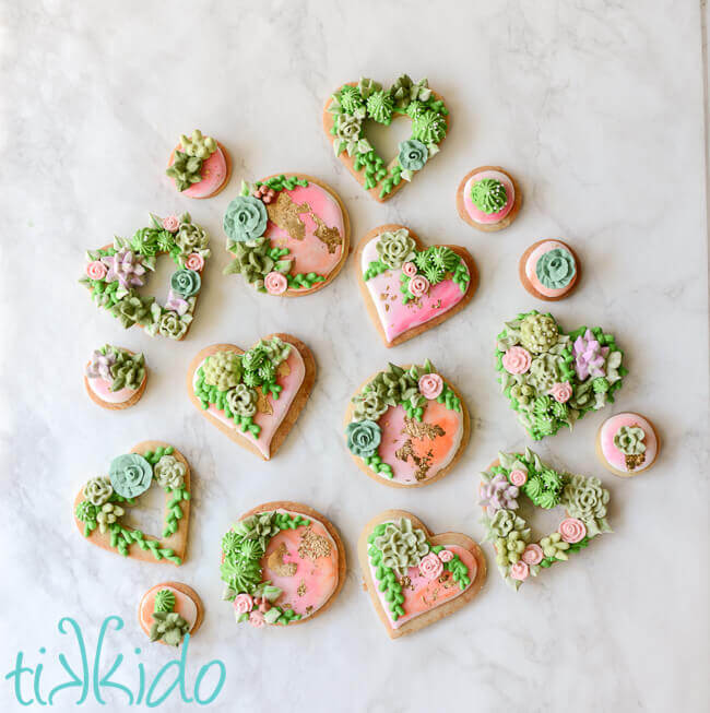 Heart and round shaped sugar cookies, covered in watercolor painted royal icing, with gold leaf and piped succulents.