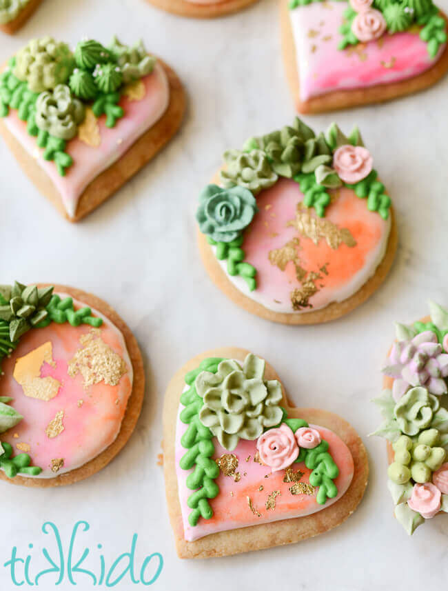 Heart and round shaped sugar cookies, covered in watercolor painted royal icing, with gold leaf and piped succulents.